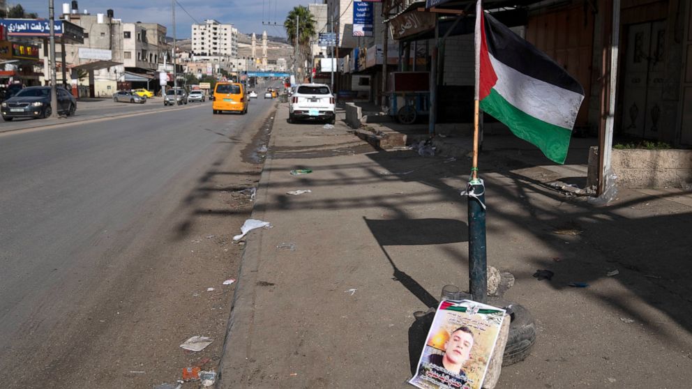 A Palestinian flag and a poster showing Ammar Adili, 22, who was shot and killed by an Israeli border police officer on Friday, mark the location of the incident, on the main thoroughfare where shops are closed in a general strike, in the West Bank t