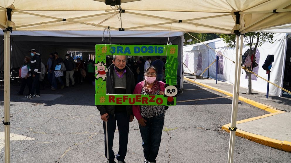 FILE - A couple poses for a photo holding a frame with a message that reads in Spanish: "Third dose, get vaccinated, reinforcement", after receiving an AstraZeneca booster against COVID-19 during a vaccination campaign for people 60 and over, in Mexi