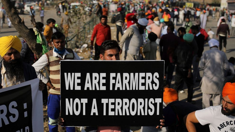 FILE- A protesting farmer holds a placard on a major highway at the Delhi-Haryana state border, India, Saturday, Nov. 28, 2020. India’s Prime Minister Narendra Modi made a surprise announcement Friday, Nov. 19, 2021. that he will withdraw the controv