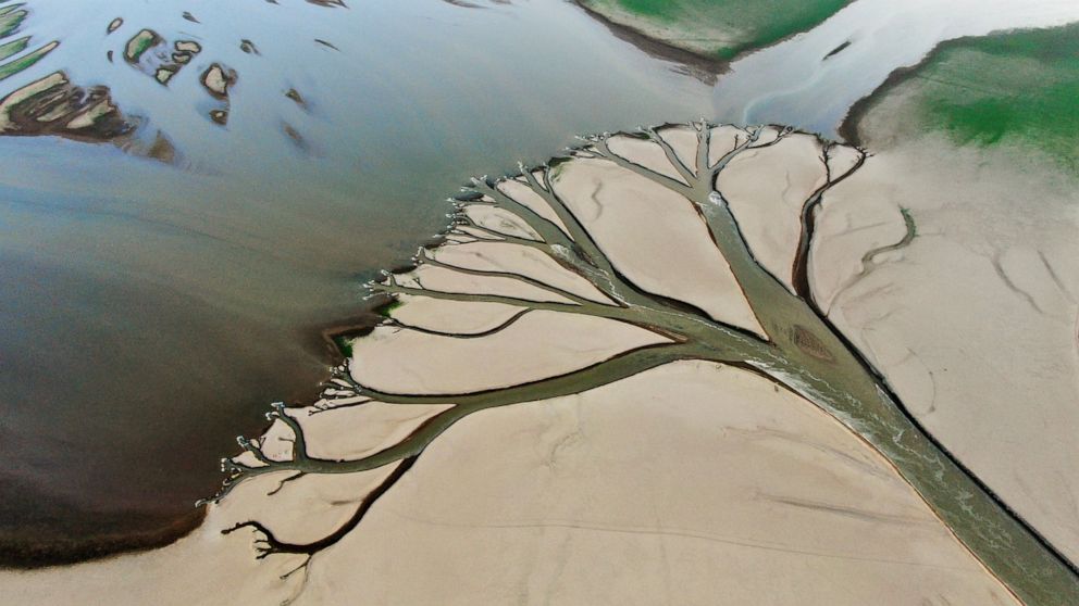 In this aerial photo released by China's Xinhua News Agency, water flows through chanels in the lake bed of Poyang Lake, China's largest freshwater lake, in eastern China's Jiangxi Province, Monday, Aug. 22, 2022. With China's biggest freshwater lake