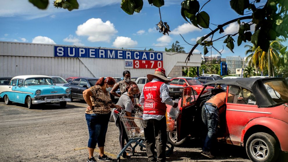 Shoppers wearing protective facemasks amid the spread of the new coronavirus load groceries from a dollar store in Havana, Cuba, Monday, July 20, 2020. Cuba has expanded the types of stores that accept dollars for payment to include food stores, as p