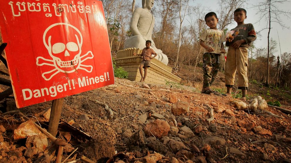 FILE - Children play near a landmine warning and a Buddhist shrine in New Village Border, Cambodia, March 10, 2005, along the Thai border. A land mine-detecting rat in Cambodia who received a prestigious award for his life-saving duty has died in ret