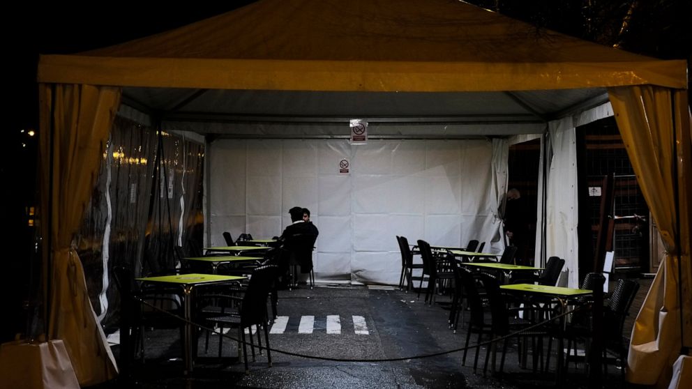Two persons seated in a terrace close to service tables empty by new measures to prevent the spread of the coronavirus, in Pamplona, northern Spain, Thursday, Jan. 27, 2021. (AP Photo/Alvaro Barrientos)