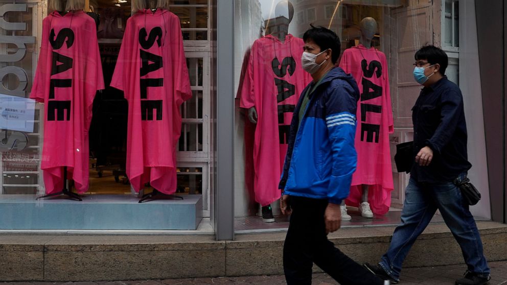People wearing face masks walk past a fashion shop in Hong Kong, Thursday, Feb. 6, 2020. Ten more people were sickened with a new virus aboard one of two quarantined cruise ships with some 5,400 passengers and crew aboard, health officials in Japan s