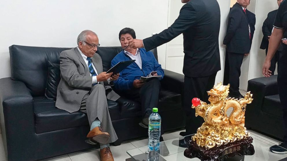 In this photo provided by Peru's police administration office, former President Pedro Castillo, second from left, and former Prime Minister Anibal Torres, far left, sit as prosecutor Marco Huaman stands at center inside a police station, where Castil