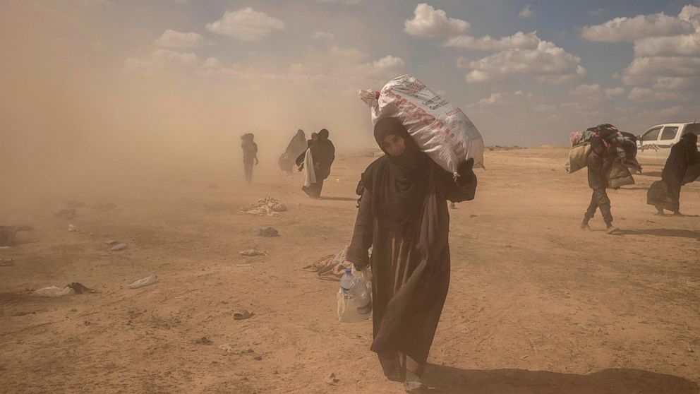 In this Wednesday, March 6, 2019, photo, a woman carries supplies from a reception area for people evacuated from the last shred of territory held by Islamic State militants, outside Baghouz, Syria. (AP Photo/Gabriel Chaim)