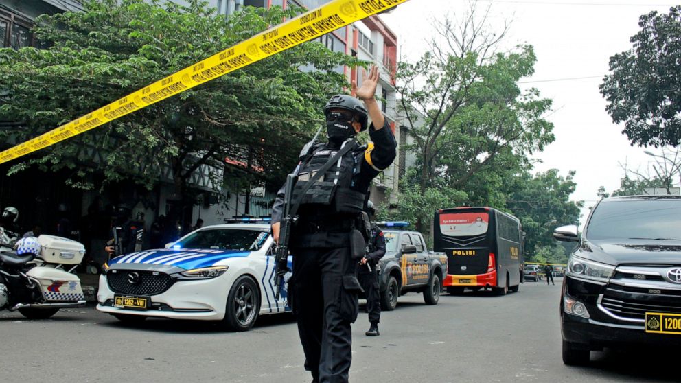A police officer gestures at the crowd to move back as he guards a road leading to a police station where a bomb exploded in Bandung, West Java, Indonesia, Wednesday, Dec. 7, 2022. A man blew himself up Wednesday at a police station on Indonesia's ma