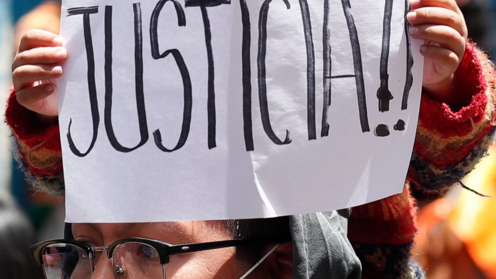 A child holds a sign reading in Spanish "Justice!" as people protest against Bolivia's former Interim President Jeanine Anez outside the police station where she is being held in La Paz, Bolivia, Sunday, March 14, 2021. Anez, who led Bolivia for a ye