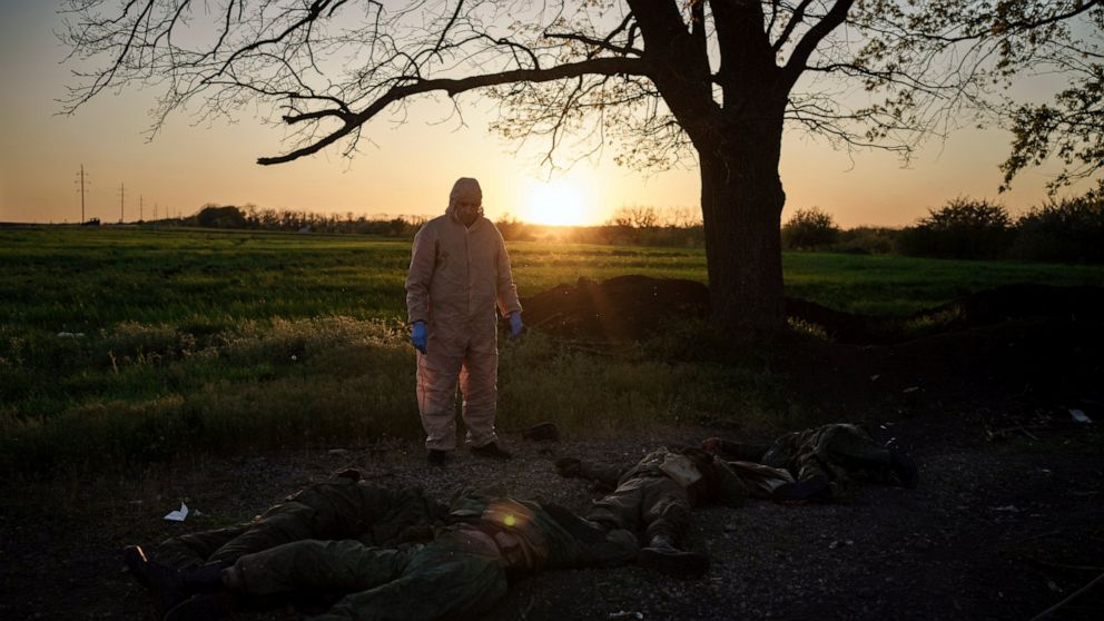 A Ukrainian emergency worker stands next to the bodies of Russian soldiers in the village of Vilkhivka, recently retaken by Ukrainian forces near Kharkiv, Ukraine, Monday, May 9, 2022. (AP Photo/Felipe Dana)