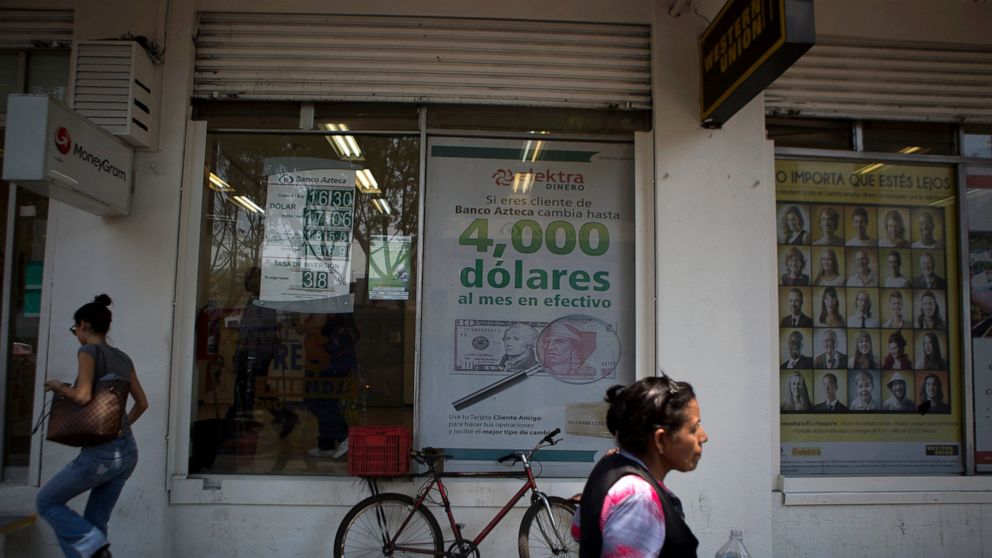 FILE - In this April 5, 2016 file photo, pedestrians walk past signs advertising money transfer services and loans, outside a business in Mexico City. Mexican migrants working abroad sent home a record $36 billion in remittances in 2019, the country'