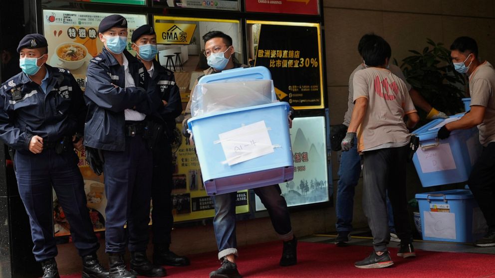 Workers carry some evidences walks past police officers outside office of "Stand News" in Hong Kong Wednesday, Dec. 29, 2021. Hong Kong police raided the office of the online news outlet on Wednesday after arresting several people for conspiracy to p