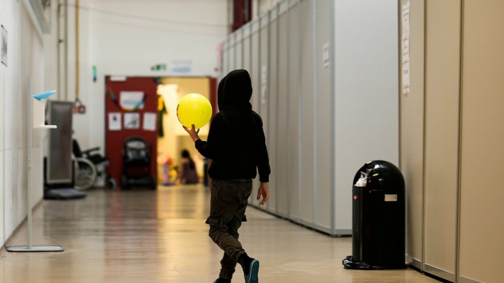 A boy with a ball walks alongside makeshift sleeping units inside the temporary refugee shelter at the former airport Tegel in Berlin, Germany, Wednesday, Nov. 9, 2022. The city of Berlin is turning a former airport into a temporary refugee shelter w