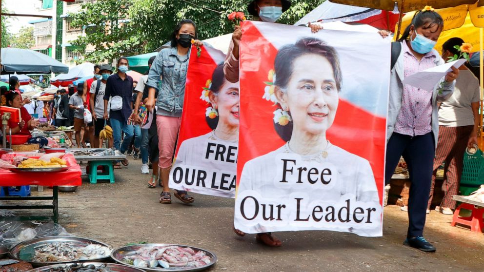 FILE - Protesters walk through a market with posters of ousted Myanmar leader Aung San Suu Kyi at Kamayut township in Yangon, Myanmar Thursday, April 8, 2021. Suu Kyi went on trial Monday, May 2, 2022, in a new corruption case against her, alleging s