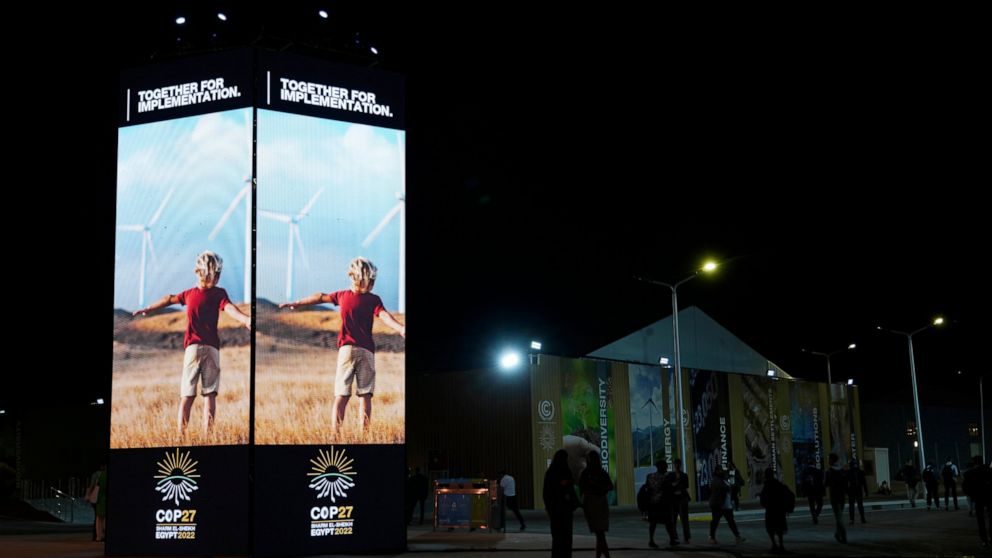 FILE - People walk past image of wind turbines at the COP27 U.N. Climate Summit, Tuesday, Nov. 8, 2022, in Sharm el-Sheikh, Egypt. (AP Photo/Peter Dejong, File)