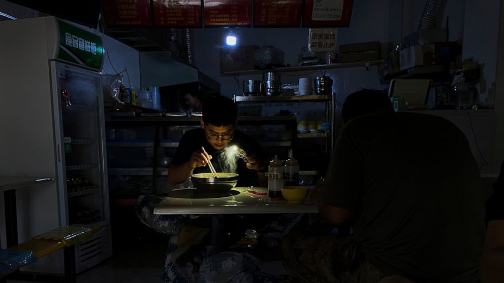 A man uses his smartphone flashlight to light up his bowl of noodles as he eats his breakfast at a restaurant during a blackout in Shenyang in northeastern China's Liaoning Province, Wednesday, Sept. 29, 2021. People ate breakfast by flashlight and s