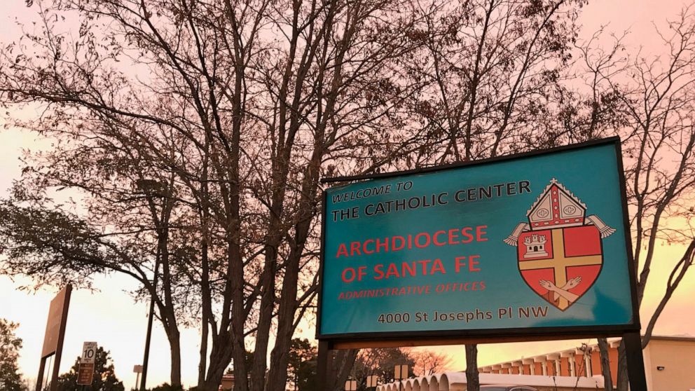 FILE - In this Nov. 29, 2018, file photo, the sun sets on a sign in front of the Archdiocese of Santa Fe offices in Albuquerque, N.M. A priest who fled the United States decades ago faces a federal trial on charges that he sexually abused a New Mexic