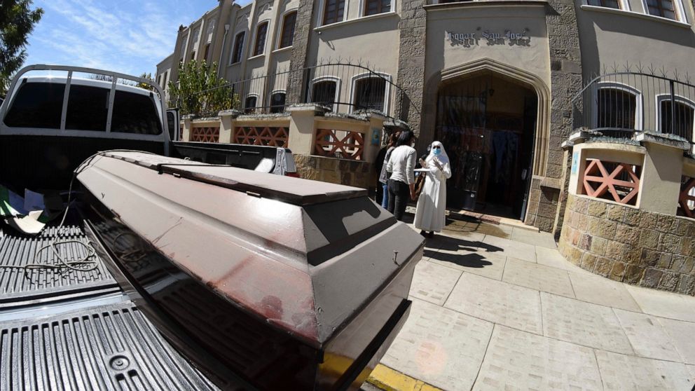 With an empty coffin in the back of their truck, health workers talk to one of the nuns that run the San Jose nursing home in Cochabamba, Bolivia, Thursday, July 16, 2020. According to city authorities, 10 elderly people with suspected COVID-19 sympt
