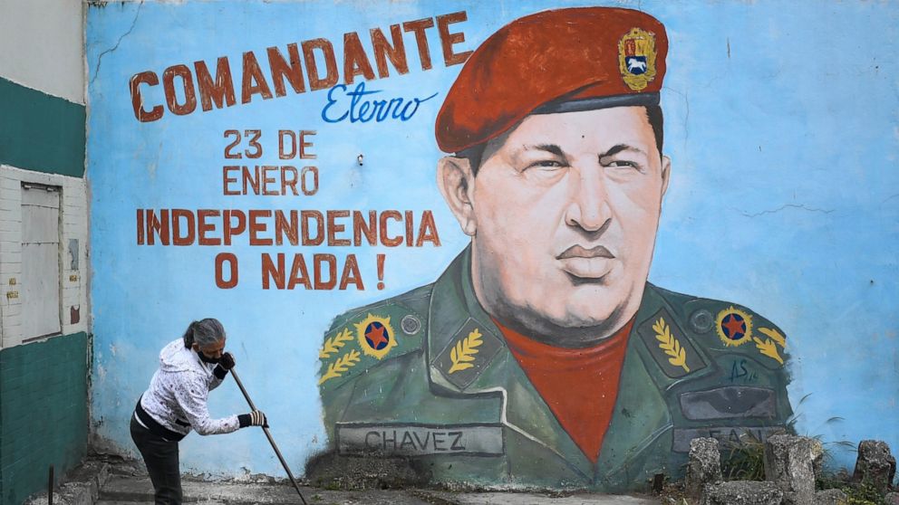 Una mujer porta una mascarilla mientras limpia una acera frente a un mural del fallecido presidente venezolano Hugo Chávez durante una jornada de limpieza y desinfección organizada por el consejo comunal y organización colectiva del vecindario 23 de 