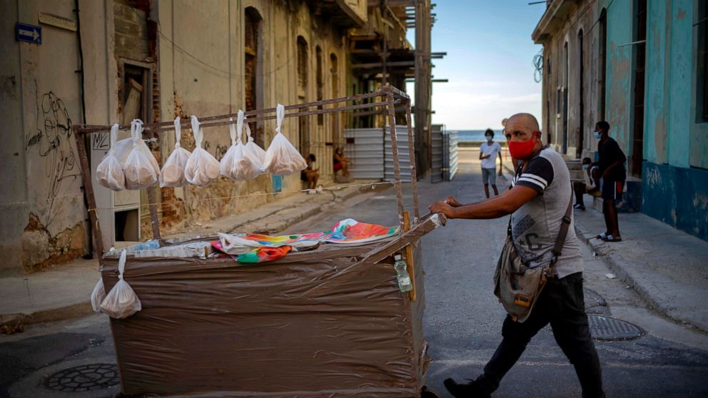 A street vendor wearing a mask as a precaution against the spread of the new coronavirus pushes his cart down a street in Havana, Cuba, Monday, Aug. 31, 2020. Cuban authorities will introduce new measures starting tomorrow Tuesday aimed at containing