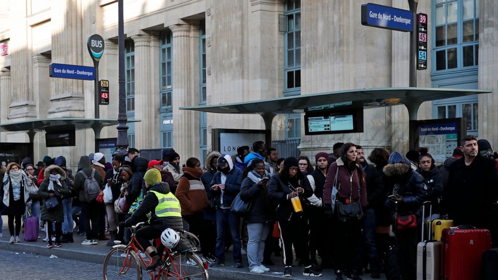A woman rides her bicycle as commuters wait for a bus at Gare du Nord Station, in Paris, Tuesday, Dec. 10, 2019. Only about a fifth of French trains ran normally Tuesday, frustrating tourists finding empty train stations, and most Paris subways were 