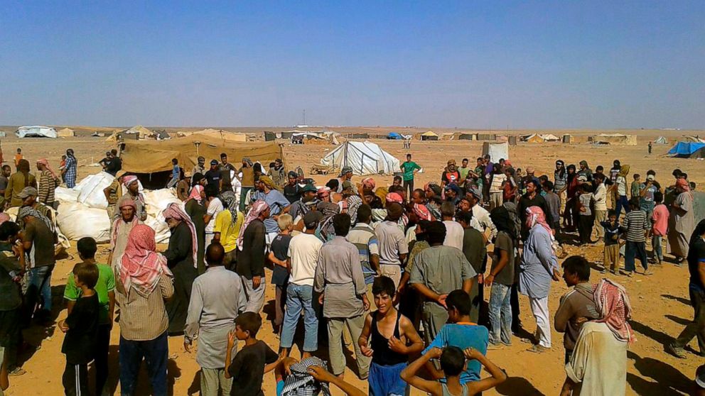 FILE - In this Aug. 4, 2016 file photo, people gather to take basic food stuffs and other aid from community leaders charged with distributing equitably the supplies to the 64,000-person refugee camp called Ruqban on the Jordan-Syria border. Over the