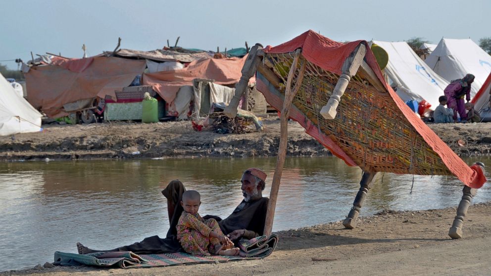 Flood victims sit under the shadow of a cot while they refuge on a roadside, in, Jaffarabad, a district of southwestern Baluchistan province, Pakistan, Monday, Sept. 19, 2022. Nearly three months after causing widespread destruction in Pakistan's cro