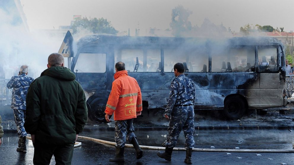 In this photo released by the Syrian official news agency SANA, Syrian firefighters and security officer check a burned bus at the site of a deadly explosion, in Damascus, Syria, Wednesday, Oct. 20, 2021. Two roadside bombs exploded near a bus carryi