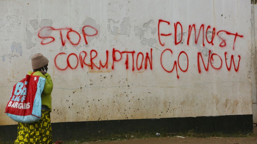 A woman walks past a wall with graffiti calling on the government to stop corruption in this Monday, June, 15, 2020 photo. Unable to protest on the streets, some in Zimbabwe are calling themselves "keyboard warriors" as they take to graffiti and soci