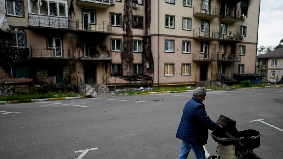 A woman walks with a baby stroller near a destroyed building during attacks in Irpin outskirts Kyiv, Ukraine, Monday, May 30, 2022. (AP Photo/Natacha Pisarenko)