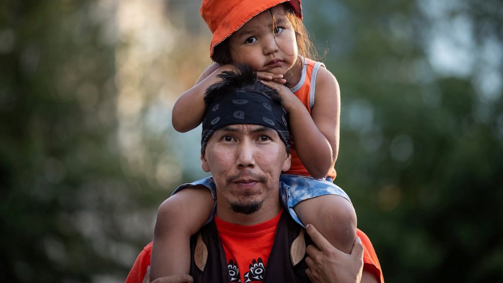 Cowichan Tribe member Benny George holds his child Bowie, 3, on his shoulders as they listen during a ceremony and vigil for the 215 children whose remains were found buried at the former Kamloops Indian Residential School, in Vancouver, British Colu