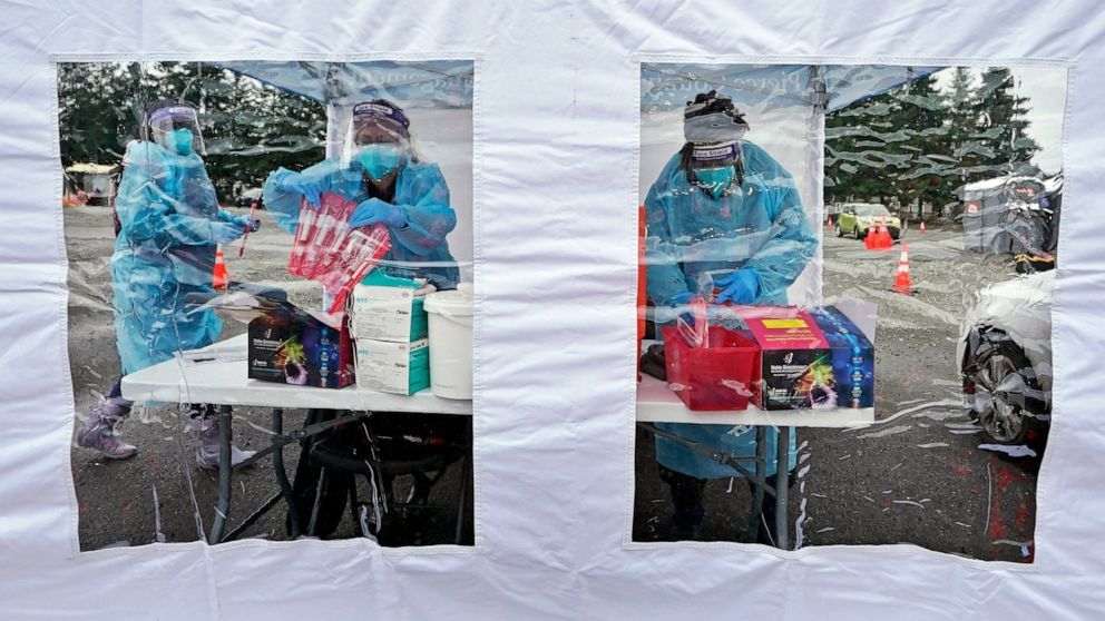 FILE - Workers at a drive-up COVID-19 testing clinic stand in a tent as they prepare PCR coronavirus tests, Jan. 4, 2022, in Puyallup, Wash., south of Seattle. Scientists are seeing signals that COVID-19′s alarming omicron wave may have peaked in Bri