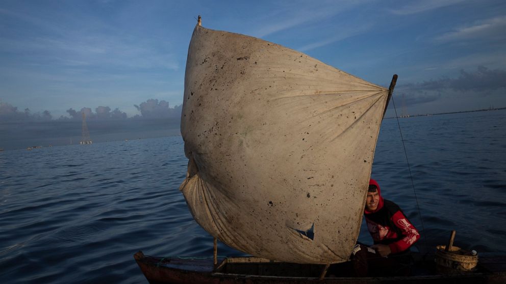Yohandry Colina uses an oil-stained sheet for a sail on the boat he uses to put fish he catches in Lake Maracaibo in Cabimas, Venezuela, Wednesday, Oct. 12, 2022. (AP Photo/Ariana Cubillos)