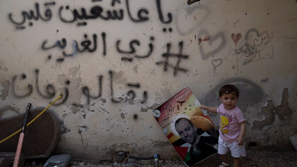 Maryam holds a poster showing her father Khalil Awawdeh, a Palestinian prisoner in Israel, at the family house in the West Bank village of Idna, Hebron, Tuesday, Aug. 9, 2022. Arabic graffiti reads: "to those who are in love, my heart is like a stran
