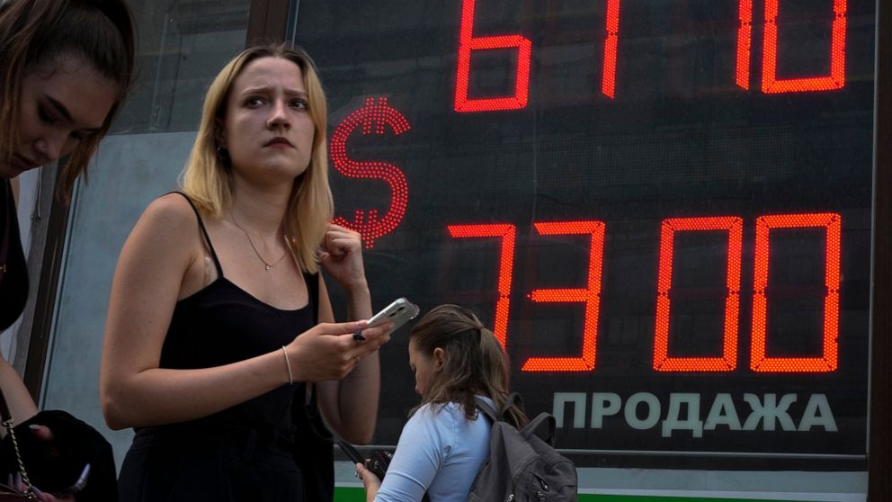 FILE - A woman walks past an exchange office screen showing the currency exchange rates of U.S. Dollar to Russian Rubles in St. Petersburg, Russia, July 5, 2022. The Russian central bank has slashed its key interest rate just a month after dropping i
