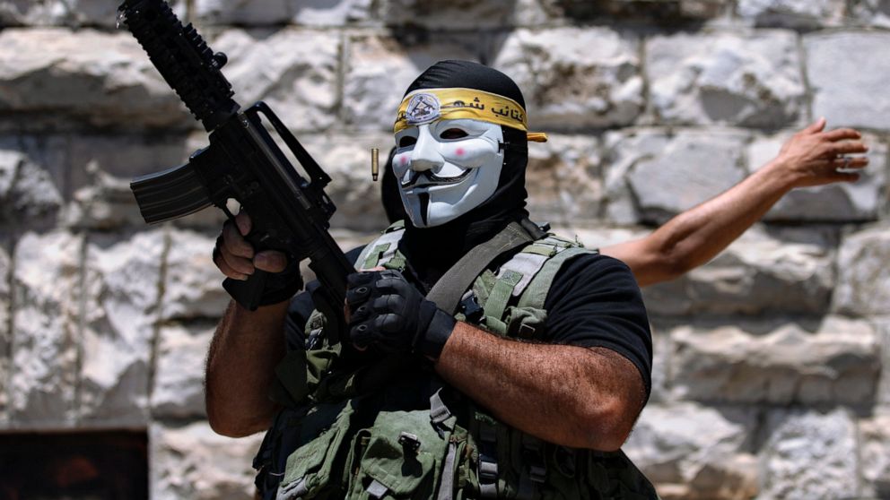 A masked Palestinian protester shoots in the air following the funeral of Mohammed al-Alami, 12, in the village of Beit Ummar, near the West Bank city of Hebron, Thursday, July 29, 2021. Villagers say the boy was fatally shot by Israeli troops while 