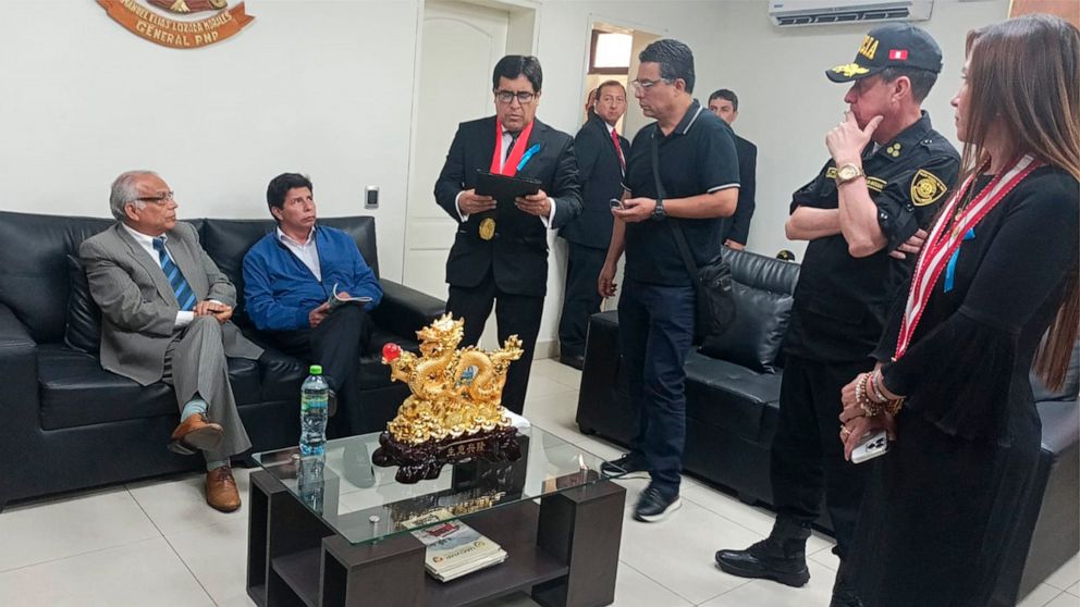 In this photo provided by Peru's police administration office, former President Pedro Castillo, second from left, and former Prime Minister Anibal Torres, far left, sit as prosecutor Marco Huaman stands at center inside a police station, where Castil