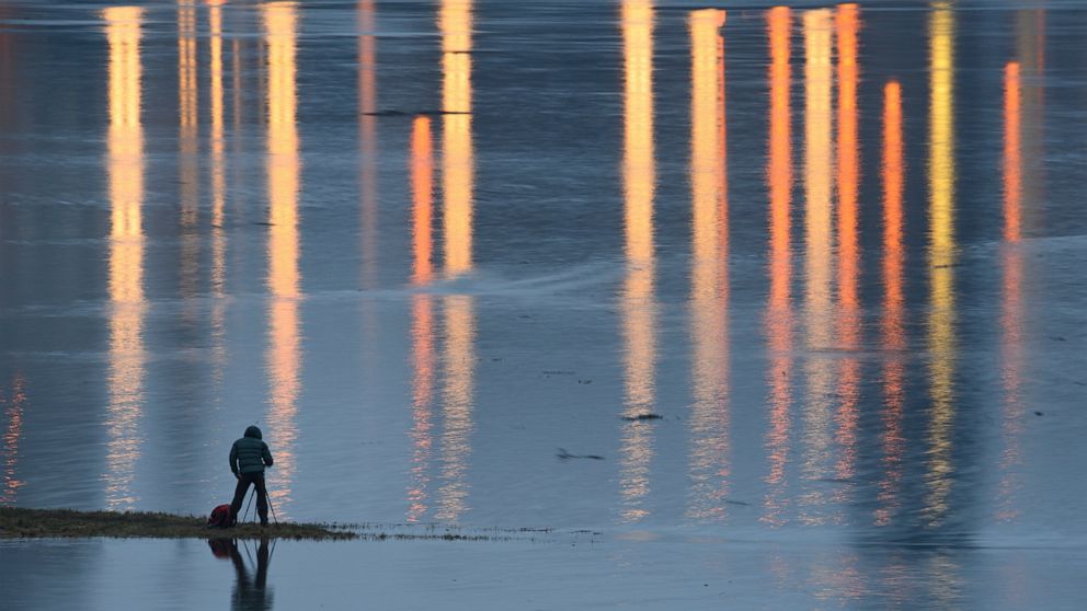 A man takes pictures of the flooded meadows near the river Elbe in Dresden, Germany, Friday, Feb. 5, 2021. (Robert Michael/dpa via AP)