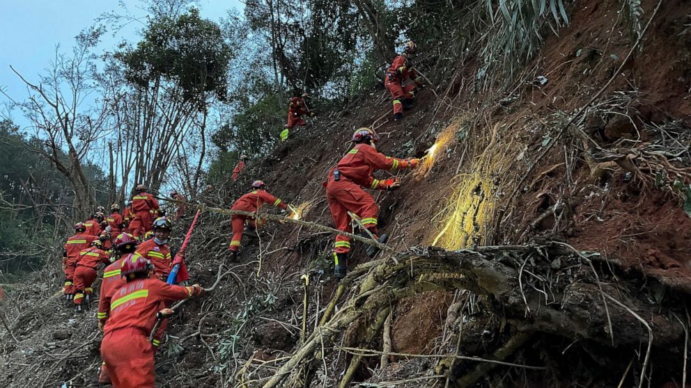 In this photo released by Xinhua News Agency, rescuers conduct search operations at the site of a plane crash in Tengxian County in southern China's Guangxi Zhuang Autonomous Region, Tuesday, March 22, 2022. Mud-stained wallets. Bank cards. Official 