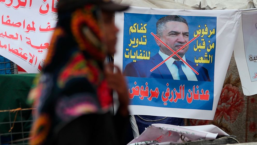 An anti-government protester passes a defaced picture of Iraq's Prime Minister-designate Adnan Al-Zurfi in Tahrir Square, Baghdad, Iraq, Wednesday, March 18, 2020. Iraq's president named Al-Zurfi as prime minister-designate, following weeks of politi