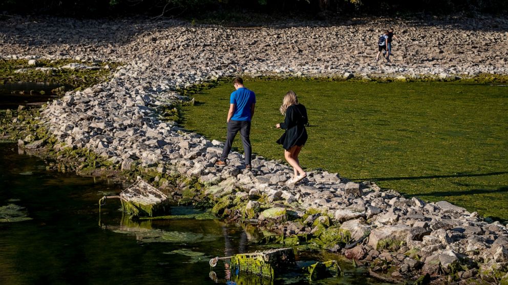 People walk over a stone dam, that is normally covered by water, towards the "Maeuseturm" (mice tower) in the middle of the river Rhine in Bingen, Germany, Friday, Aug. 12, 2022. The Rhine carries low water after a long drought period. (AP Photo/Mich
