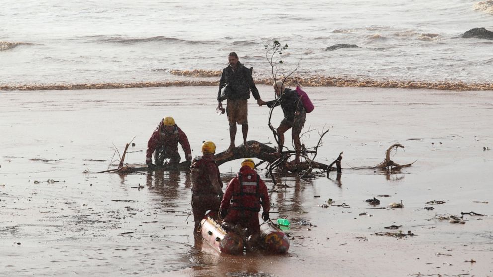 A couple, centre, attempt to make their way through muddy waters on a beach near Durban, South Africa, Sunday, May 22, 2022. More than 300 people have been evacuated from their homes as a result of renewed heavy rains, flooding and mudslides in South