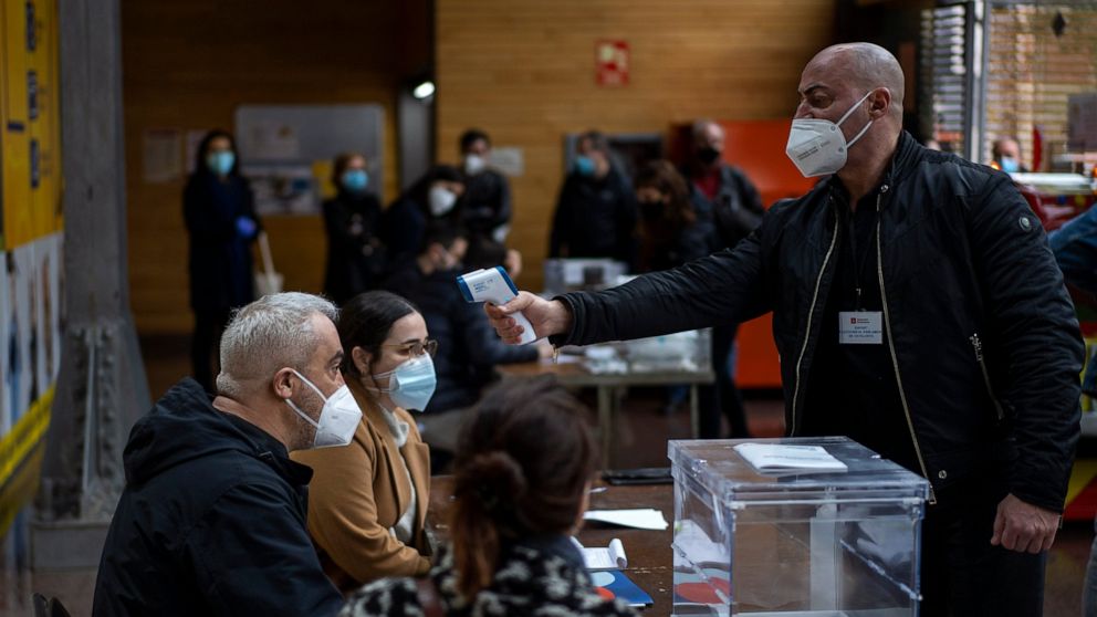 A man working at a polling station set up in a market, is taken the temperature during the regional Catalan election in Barcelona, Spain, Sunday, Feb. 14, 2021. Over five million voters are called to the polls on Sunday in Spain's northeast Catalonia