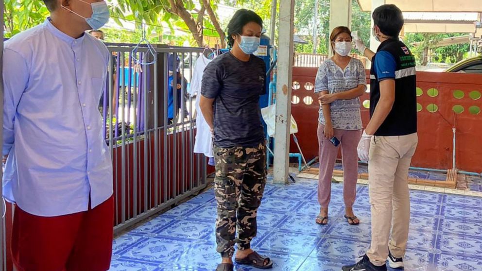 In this photo released by the San Sai District Administrative Office, a Thai officer checks the temperature of journalists working for Democratic Voice of Burma, at San Sai District in Chiang Mai province north of Thailand Sunday, May 9, 2021. Three 