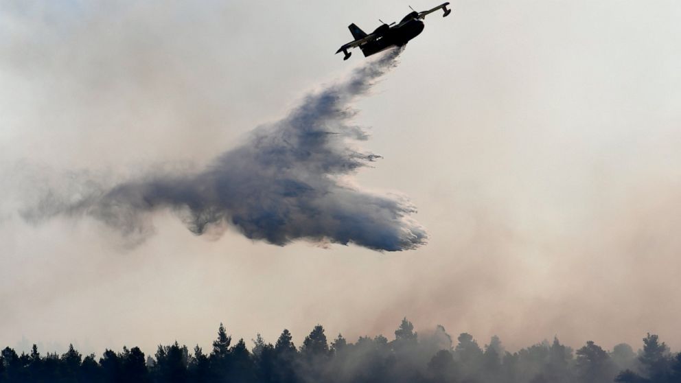 An airplane drops water over a wildfire near Halkida town on the Greek island of Evia, Wednesday, Aug. 14, 2019. More than a thousand firefighters battled wildfires Tuesday in Greece, with the largest burning out of control through a nature reserve o