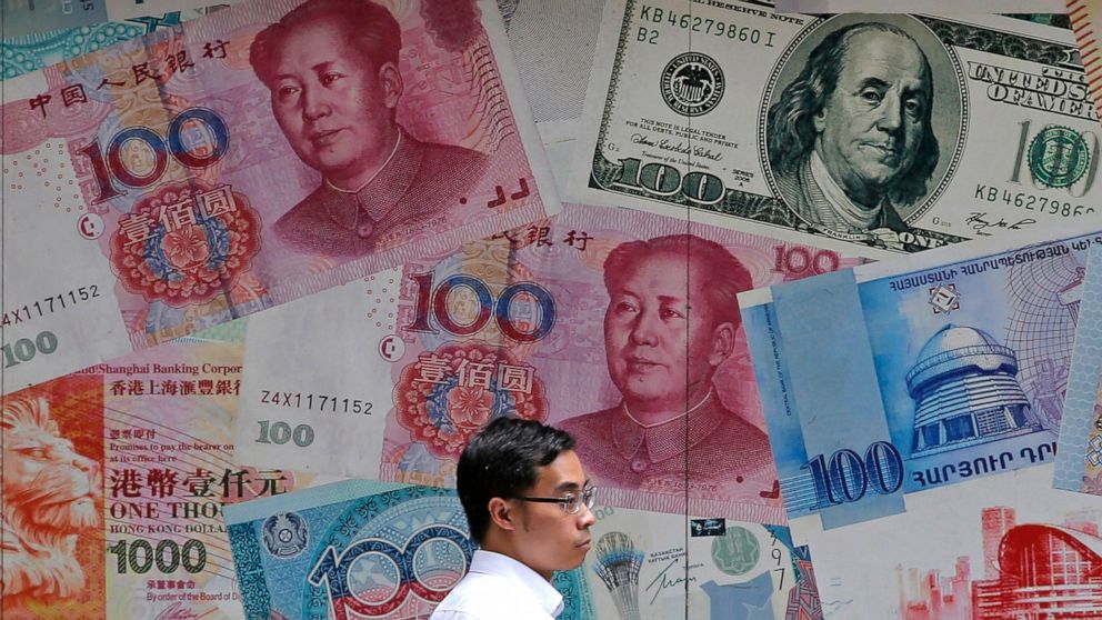 FILE - In this June 10, 2019, file photo, a man walks past a money exchange shop decorated with different banknotes at Central, a business district of Hong Kong. China's yuan fell below the politically sensitive level of seven to the U.S. dollar on M
