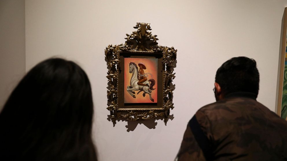People watch a painting showing 1910-17 Mexican revolutionary hero Emiliano Zapata nude, wearing high heels and a pink, broad-brimmed hat, straddling a horse, in Mexico City, Tuesday, Dec. 10, 2019. The work by Fabian Chairez is part of an exhibit ab