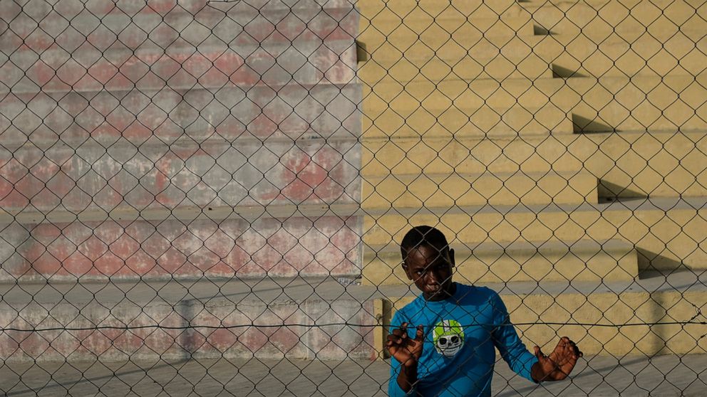 A youth stands at a gate on a dirt field at the Hugo Chavez Square in Port-au-Prince, Haiti, Thursday, Oct. 28, 2021. (AP Photo/Matias Delacroix)