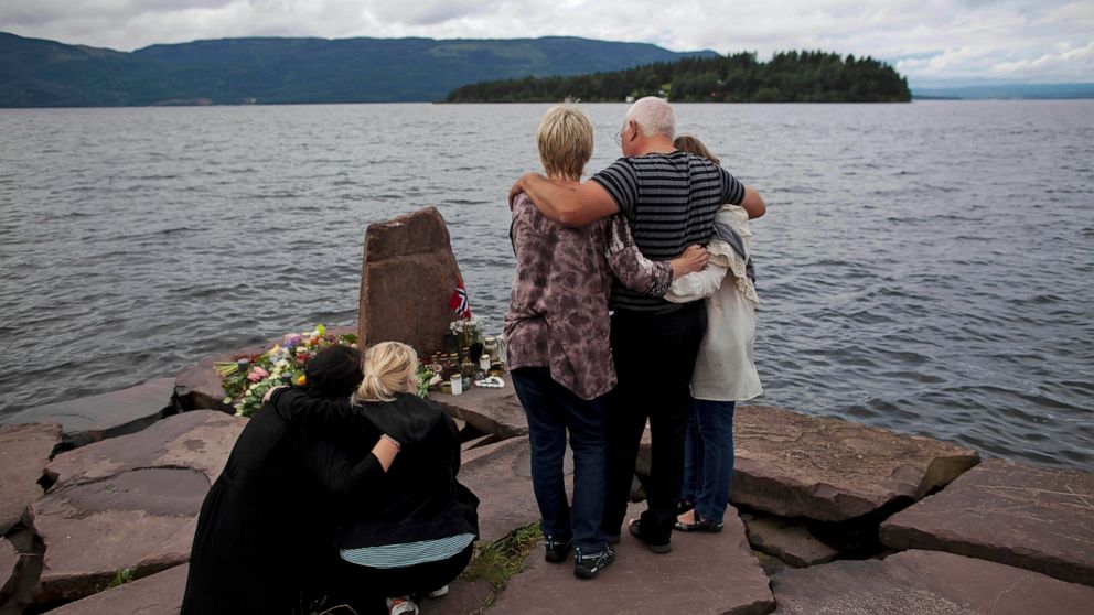 FILE - In this Monday, July 25, 2011 file photo, relatives of a victim gather to observe a minute's silence on a campsite jetty on the Norwegian mainland, across the water from Utoya island, seen in the background, where people have been placing flor