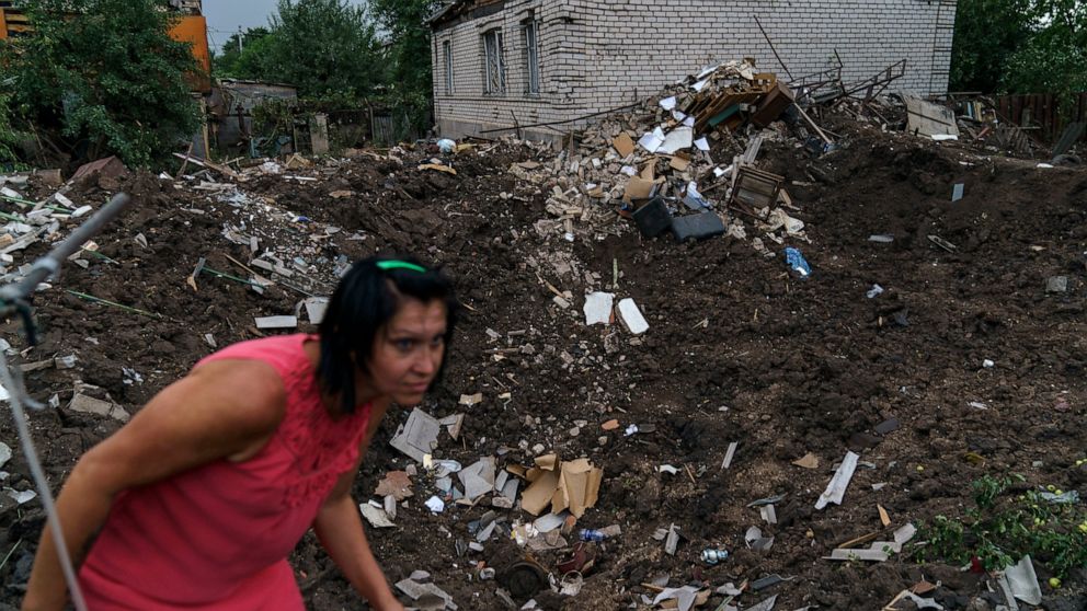 Olga Rudneva walks along the edge of a crater Thursday, Aug. 18, 2022, from a rocket strike yesterday in Druzhkivka, Donetsk region, eastern Ukraine, as Russian shelling continued to hit towns and villages in Donetsk province, regional officials said