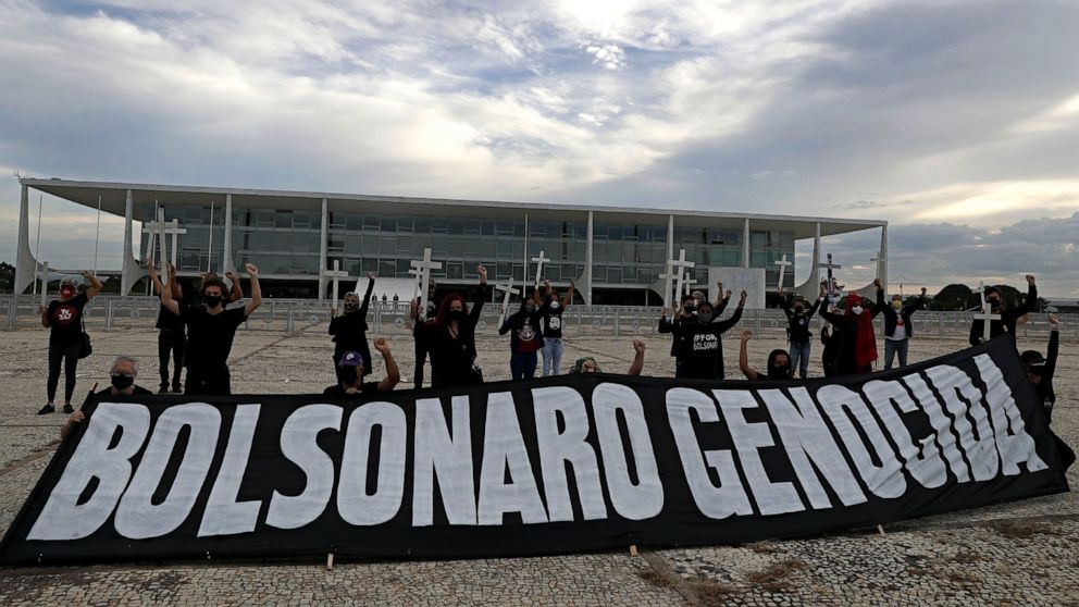 Demonstrators hold crosses to represent people who have died of COVID-19 behind the Portuguese phrase "Bolsonaro genocide" as they protest the president's handling of the COVID-19 pandemic outside Planalto presidential palace in Brasilia, Brazil, Fri